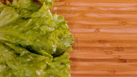 Téléchargez les photos : TOP DOWN, CLOSE UP, COPY SPACE: Cinematic shot of glassy water droplets flying as wet iceberg hits the chef's cutting board. Wet romaine lettuce leaves fall onto the empty wooden chopping board. - en image libre de droit