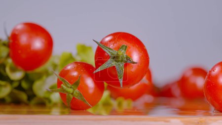 Foto de MACRO, DOF: Sweet cherry tomatoes roll around the wet chopping board while chef is making a salad. Washed organically grown salad ingredients are rolling around the empty wooden kitchen countertop. - Imagen libre de derechos