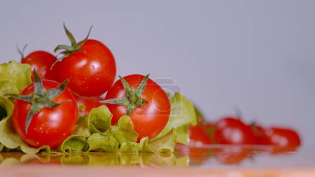 Foto de COPY SPACE, MACRO, DOF: Small round cherry tomatoes fall onto wet romaine lettuce leaves sitting on the chef's chopping board. Delicious washed salad ingredients rolling around a kitchen countertop - Imagen libre de derechos
