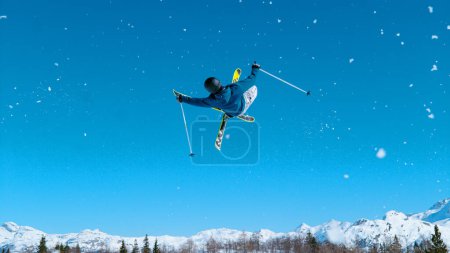 Téléchargez les photos : Young male tourist on skiing trip rides around the fun park and does breathtaking tricks. Freestyle skier takes off the kicker and does a difficult high flying 360 grab. Athletic traveler skiing. - en image libre de droit
