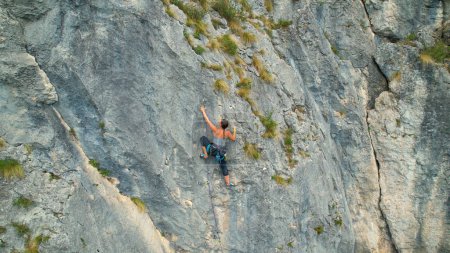 Téléchargez les photos : AÉRIAL : Spectaculaire vue par drone d'une grimpeuse sportive montant une falaise difficile. Voler haut au-dessus d'une jeune femme courageuse voyageant à travers l'Europe pour escalader les falaises les plus dures. - en image libre de droit