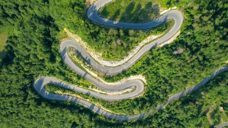 Téléchargez les photos : AÉRIAL, TOP DOWN : La route de basculement vide serpente vers le haut d'une colline et à travers une forêt luxuriante. Voler au-dessus d'une route de montagne asphaltée pleine de virages serrés en épingle à cheveux traversant les bois animés de Slovénie - en image libre de droit