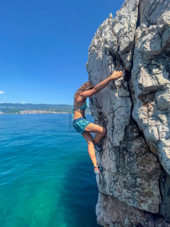 Photo for CLOSE UP: Female climber deep water solo climbing above clear blue seawater. Picturesque seaside location for sports activity. Sporty woman bouldering on active and adventurous summer holidays. - Royalty Free Image
