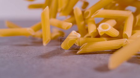 Photo for Whole bunch of pasta pennette rigate in mid-air on grey background. Right side throw of falling penne pasta in mid-air. Detailed view of flying Italian uncooked pasta rigatoni. - Royalty Free Image