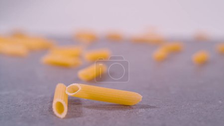 Foto de Detailed view of raw italian pasta rigatoni on grey background. Diagonaly cut pasta pennette rigate with ridged surface. Important cooking ingredient in italian cuisine. - Imagen libre de derechos
