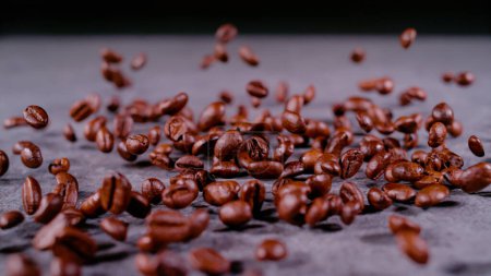 Téléchargez les photos : CLOSE UP, BOKEH: Evenly scattered pile of coffee grains bouncing from surface on gray background. Roasted brown coffee seeds caught in motion. Detailed view of flying coffee source with shallow focus. - en image libre de droit
