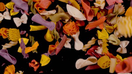 Photo for Pasta in many shapes and colours falling on black background. Abstract view of scattered coloured pasta mixture. Detailed view of several sorts of Italian raw pasta in shallow focus. - Royalty Free Image