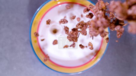 Foto de CLOSE UP, BOKEH: Centered top down view of chocolate granola splashing in milk bowl. Healthy homemade muesli in shallow focus falling in milk bowl. Detailed view of delicious breakfast assembly. - Imagen libre de derechos