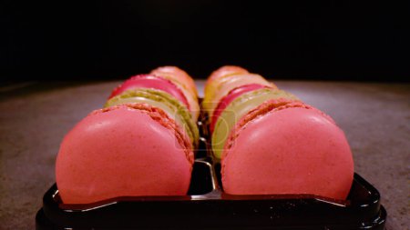 Téléchargez les photos : CLOSE UP, BOKEH: Lined up delicious sweet French macarons in pastel pink colours. Tasty confectionery in bright colours on black background. Delicious macarons of different flavors and colors in a row - en image libre de droit