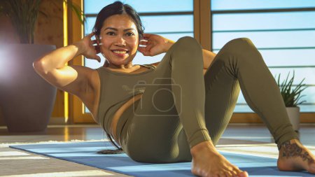 Téléchargez les photos : Cheerful Philippine lady performing sport exercises for core strength. Pretty woman during abdominal muscles workout training. Young female in sportswear at fitness activity for staying fit. - en image libre de droit
