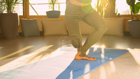 Foto de Fit young woman doing cross lunge squats in beautiful golden light. Sporty lady in sportswear during bodyweight training doing exercises for leg and lower back muscles and body stability. - Imagen libre de derechos
