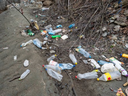 Foto de TIRANA, ALBANIA, MARCH 2022: Plastic bottles and other garbage waste lying on a sandy river shore. Sad view of polluted river bank with plastic garbage. Urgent need to raise environmental awareness. - Imagen libre de derechos