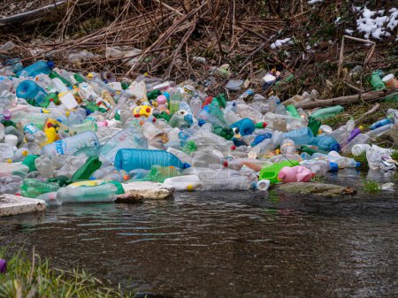 CLOSE UP: Accumulated pile of various plastic bottles caught at the river edge. Worrying view of the polluted river with thrown plastic rubbish. Accumulated plastic bottles floating on river surface.