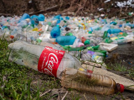 Téléchargez les photos : TIRANA, ALBANIA, MARCH 2022: Ironic text on plastic Coca Cola bottle near waste pollution at river. Inappropriate place for garbage disposal. Accumulated plastic garbage floating on the river surface. - en image libre de droit