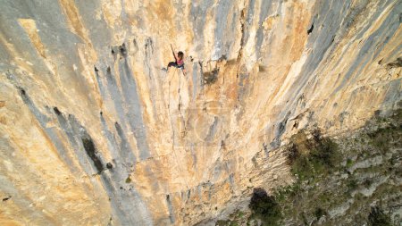 Photo for AERIAL: Sporty young woman top rope climbing up the picturesque limestone wall. Adrenaline outdoor activity in breathtaking and picturesque surroundings. Rock climber on the way up of canyon wall. - Royalty Free Image