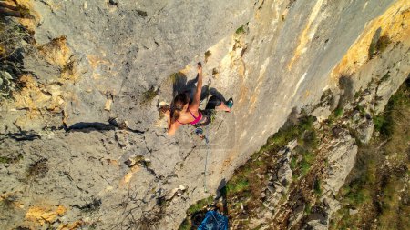 Téléchargez les photos : AERIAL: View of young sporty woman lead climbing up the gorgeous limestone wall. Female rock climber on her way up the rock climbing wall. Adrenaline sport activities in beautiful outdoor environment. - en image libre de droit