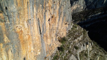 Photo for AERIAL: Sporty young woman climbing in the middle of the sunlit limestone wall. Adrenaline outdoor activity in beautiful and picturesque environment. Rock climber on the way up of the limestone wall. - Royalty Free Image