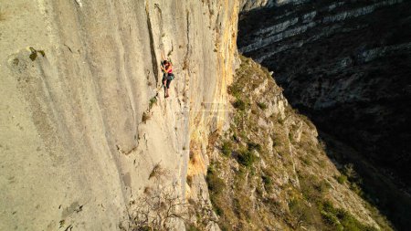 Photo for AERIAL: Young female climber lead climbing up the sunlit canyon limestone wall. Adrenaline sport activities in gorgeous outdoor environment. Female rock climber on her way up the rock climbing wall. - Royalty Free Image