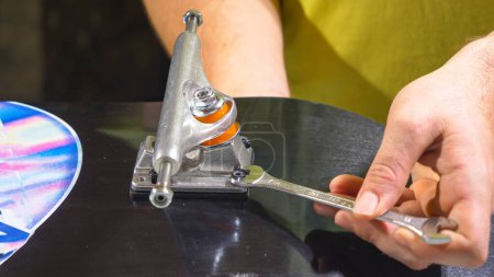 Photo for CLOSE UP: Young man firming and screwing the nut on bolt of skateboard trucks with wrench. Mistake at bolting trucks on skate deck for mounting wheels. Assembling parts for new skateboarding setup. - Royalty Free Image