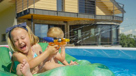 Photo for CLOSE UP: Smiling kids having fun at pool party while splashing with water blaster. Refreshing water games for hot summer days. Children laughing and enjoying splashy water activities at home garden. - Royalty Free Image