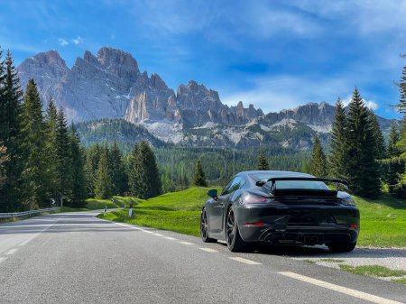 Téléchargez les photos : GIAU PASS, DOLOMITES, ITALY, MAY 2022: Black sports car at side of winding mountain road with beautiful alpine backdrop. Idyllic alpine nature in spring with forest and mountain peaks with spring snow - en image libre de droit