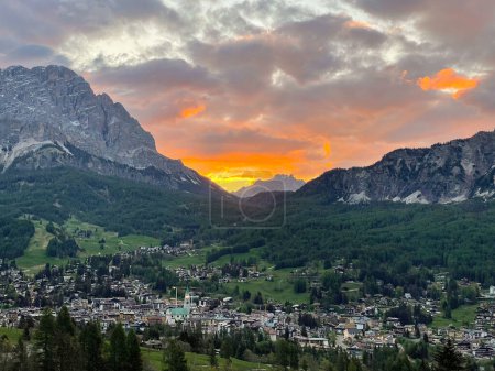 Foto de Beautiful sunset view above city in the embrace of alpine mountains in Dolomites. Glowing colorful skyscape above high mountain peaks and town in the valley. Picturesque moment at the end of the day. - Imagen libre de derechos