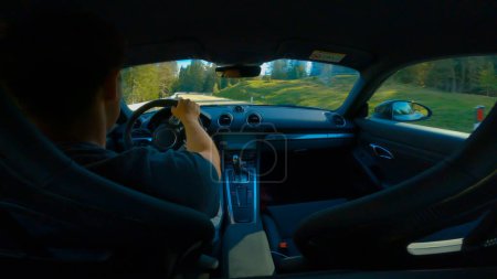 Foto de GIAU PASS, DOLOMITES, ITALY, MAY 2022: Young man on a drive through serpentine bends along a winding mountain pass road. Back seat view of drive along curved alpine road surrounded with green forest. - Imagen libre de derechos