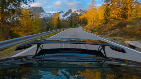 Téléchargez les photos : GIAU PASS, DOLOMITES, ITALY, MAY 2022: Amazing scenic view with sports car spoiler at serpentine road at golden hour. Picturesque gold-lit alpine landscape while driving downhill on a mountain road. - en image libre de droit
