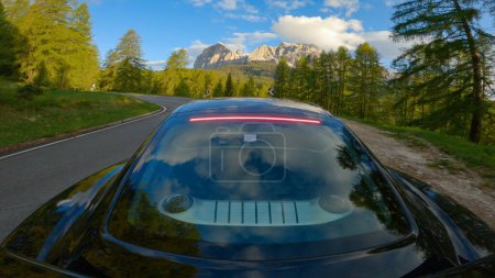 Téléchargez les photos : GIAU PASS, DOLOMITES, ITALY, MAY 2022: Car drive along alpine road through green forest with amazing views of mountains. Travelling through gorgeous scenic alpine landscape in spring on a sunny day. - en image libre de droit