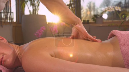 Foto de Golden sunlight shines through female hands while performing back massage. Detailed view of young woman's working hands during body massage. Relaxing wellness treatment at the end of the day - Imagen libre de derechos
