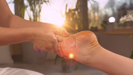 Téléchargez les photos : Reflexology therapy practice for stress relief in nice golden light. Relaxing wellness treatment at the end of the day. Sun shinning through massaging hands while performing reflexotherapy. - en image libre de droit