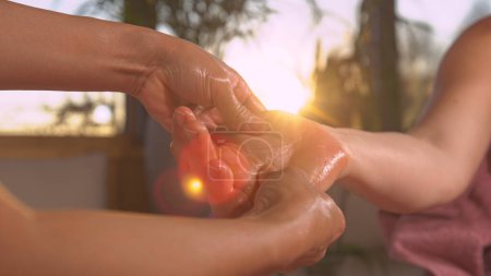 Foto de Female therapist performing hand reflexology massage in golden light. Reflexology therapy for stress relief and helping body work better. Relaxing wellness treatment at the end of the day. - Imagen libre de derechos