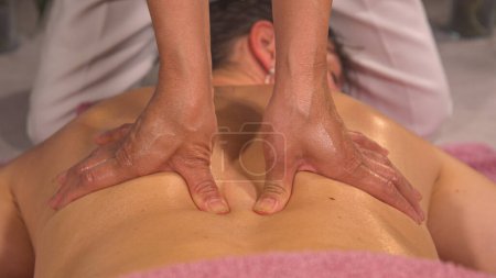 Téléchargez les photos : Professional massage therapist is treating a young female patient. Relaxation, beauty, body and face treatment concept. Detailed view of female hands performing back muscle relief massage. - en image libre de droit