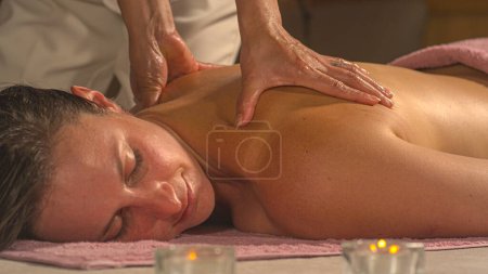 Téléchargez les photos : Pretty young woman enjoying while relaxing at therapeutic Thai massage. Female person being gently massaged by a professional therapist. Spa treatment for body harmony and stress relief. - en image libre de droit