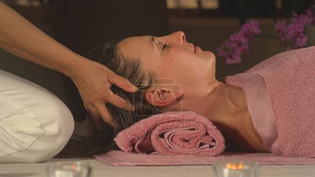 Téléchargez les photos : Beautiful woman enjoying at relaxing head massage with her eyes closed. Female person being gently massaged by a professional therapist. Spa treatment for body harmony and stress relief. - en image libre de droit