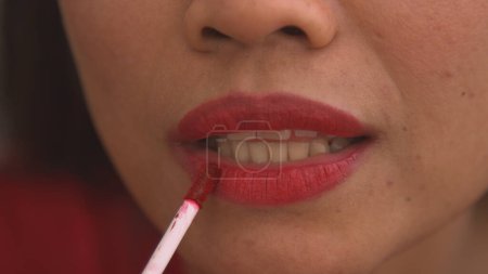Téléchargez les photos : Detailed shot of young female lips after applying shiny red lip gloss. Pretty young lady using colourful and vibrant cosmetic product for lips. Female person perfecting look using cosmetics. - en image libre de droit