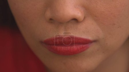 Téléchargez les photos : Detailed shot of young woman applying red lip gloss to her lips. Pretty young lady using colourful and vibrant cosmetic product for lips. Female person emphasizing her lips. - en image libre de droit