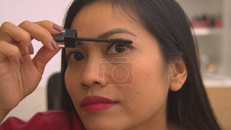 Téléchargez les photos : Detailed view of pretty Philippine woman applying mascara to eyelashes. Headshot of young lady putting on eye make up for special occasion. Female person taking care of her glamourous look. - en image libre de droit