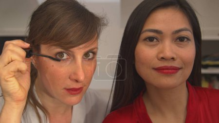 Photo for CLOSE UP: Two beautiful women using beauty products for applying face make up. Caucasian and Asian woman getting ready for a girls night out. Attractive ladies having fun while using make up products. - Royalty Free Image