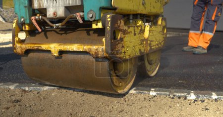 Photo for APRIL 2022, LJUBLJANA, SLOVENIA, CLOSE UP: Working with asphalt roller for compacting asphalt while paving yard. Man at work in beautiful morning light. Man in uniform asphalt paving the driveway. - Royalty Free Image