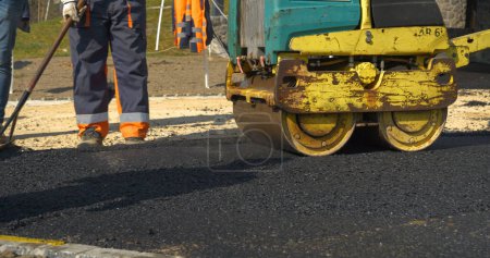 Photo for Working with asphalt roller for compacting and smoothing surface at driveway. Worker operating machinery during process of asphalting. Men in uniform asphalt paving yard in beautiful morning light. - Royalty Free Image