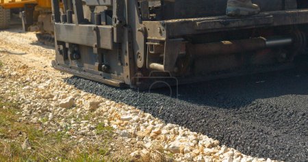 Photo for CLOSE UP: Rear view of heavy asphalt paver machine leaving fresh blacktop behind. Construction workers operating with heavy machinery for laying black asphalt surface at parking lot in morning light. - Royalty Free Image