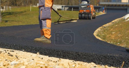 Photo for Two workers smoothing and levelling edges of freshly laid asphalt roadway bend. Construction workers working with shovel and scrapper for finishing touches of paved road in beautiful morning light. - Royalty Free Image