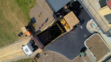 Photo for AERIAL TOP DOWN: Construction workers laying fresh asphalt on yard with driveway. Builders preparing terrain for finishing paving the roadway in morning light. Men in uniform asphalt paving driveway. - Royalty Free Image