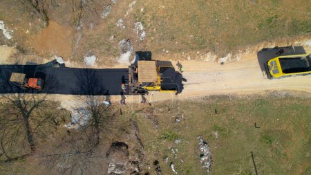 Photo for AERIAL TOP DOWN: Construction workers laying asphalt and freshly paved driveway. Builders preparing terrain for finishing paving the roadway in morning light. Roadworkers asphalt paving driveway. - Royalty Free Image