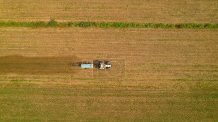 Foto de AERIAL, TOP DOWN: Farm tractor spreading manure on arable land in autumn season. White tractor with slurry spreader fertilizing agricultural field on a sunny day. Agricultural tasks in fall season. - Imagen libre de derechos