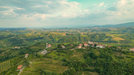 Foto de AERIAL: Beautiful village on top of small hill in the embrace of wine country. Well-kept vineyards, forest patches and idyllic small settlements scattered across picturesque hilly landscape in autumn. - Imagen libre de derechos