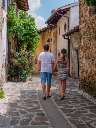 Téléchargez les photos : Young couple on romantic walk through picturesque alley of an old historic town. Rear view of woman and man holding hands while strolling along lovely stone street surrounded with old stone houses. - en image libre de droit