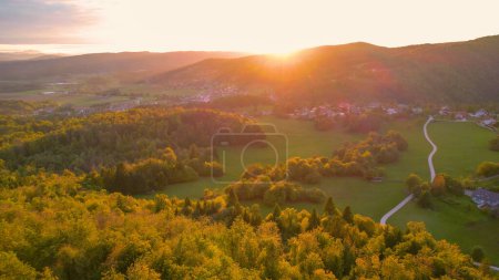 Téléchargez les photos : Picturesque hilly countryside with villages and farmland in golden light. Beautiful landscape with forested hills, green pastures and idyllic settlements bathing in last rays of autumn sun. - en image libre de droit
