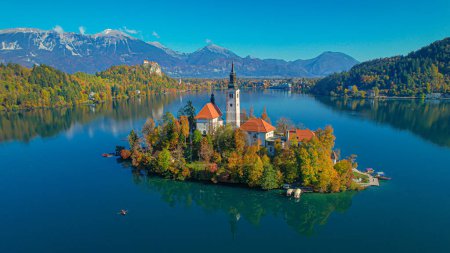 Foto de AERIAL: Amazing scenic view of famous tourist attraction lake Bled with island. Gorgeous Bled island with church in the embrace of vivid autumn trees. Beautiful fall season creating picturesque views. - Imagen libre de derechos